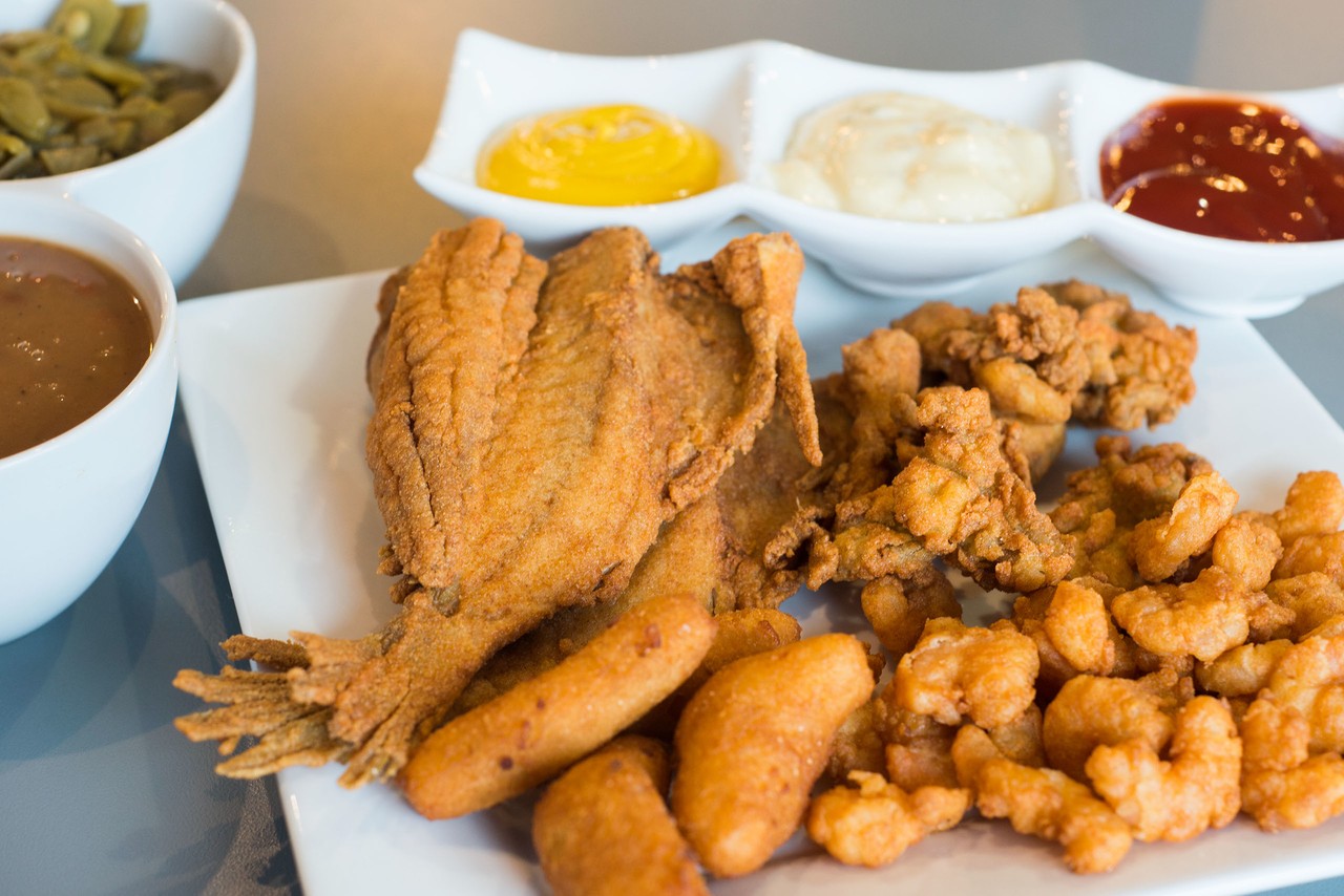 A large plate of fried shrimp and fish accompanied by dipping sauces