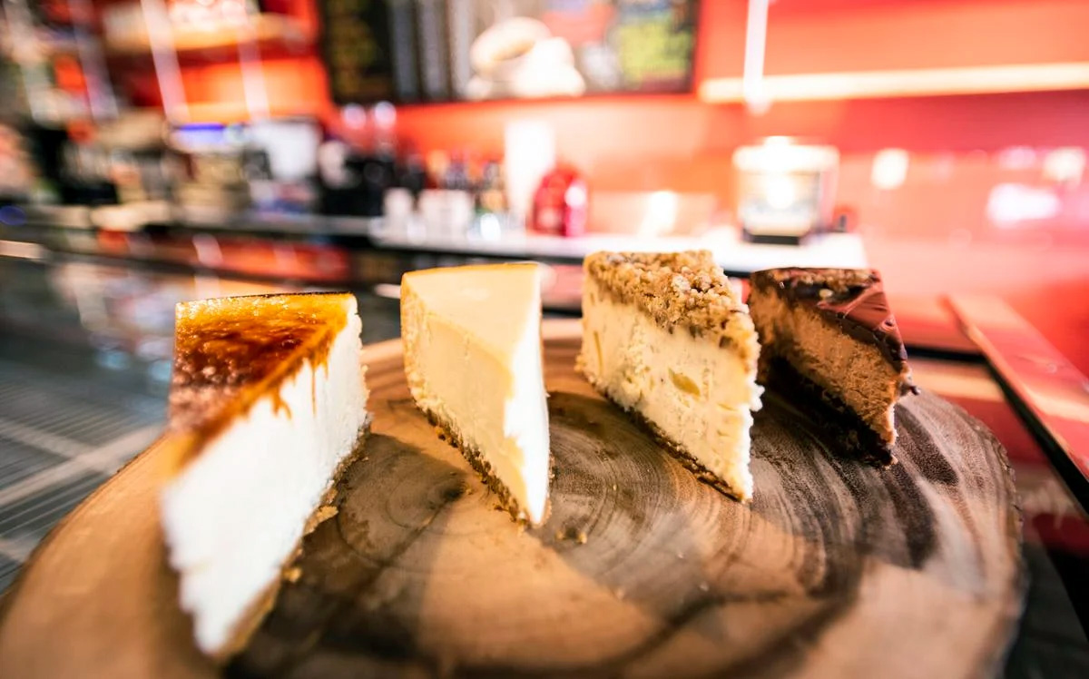 Four slices of cheesecake on a wood grain surface inside of a brightly colored bakery storefront