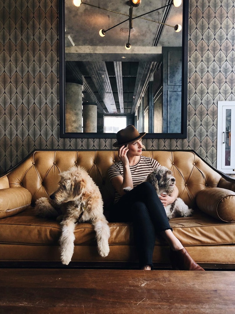 A woman sitting on a leather sofa with a dog sitting on either side at the Cardinal Hotel in Winston-Salem