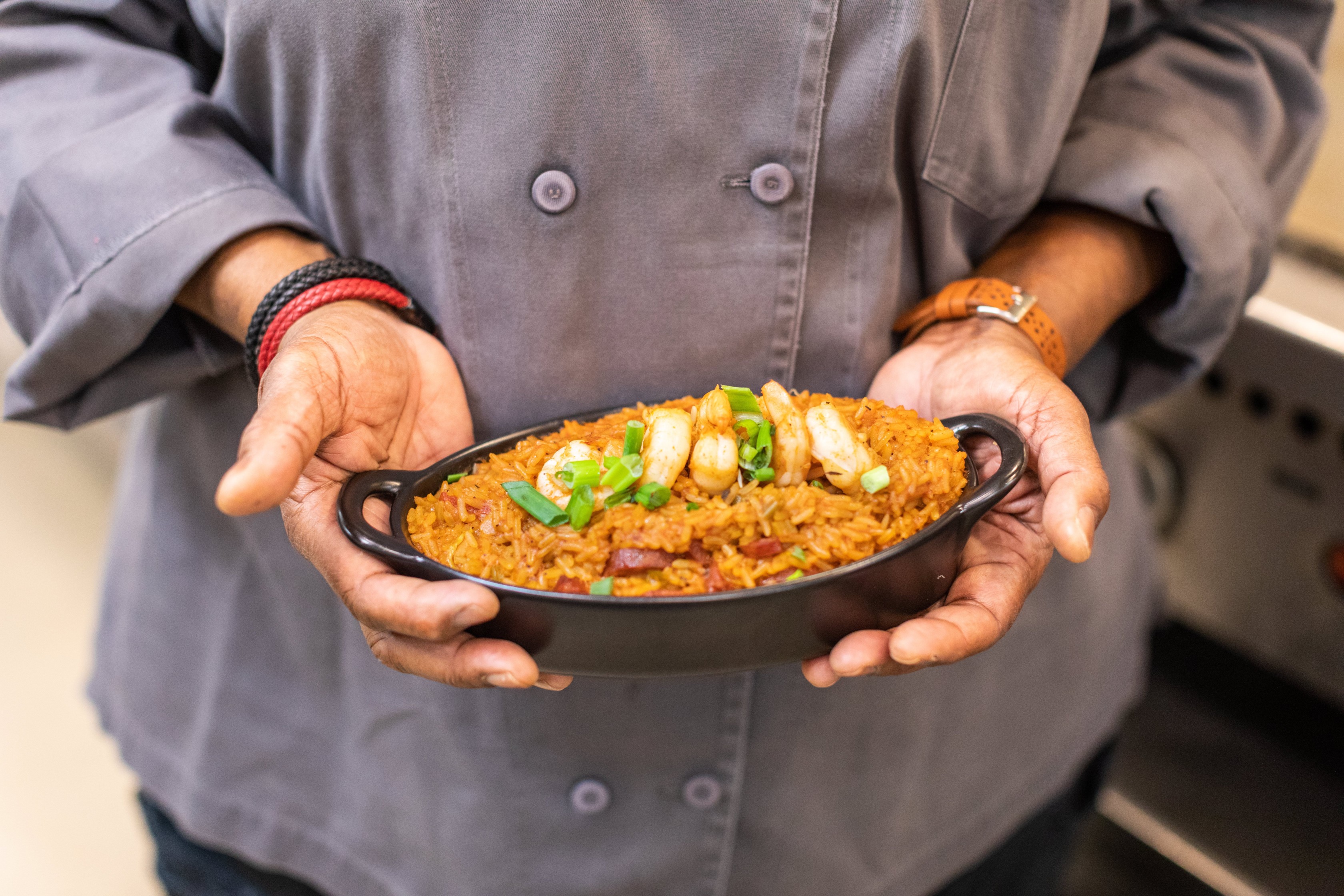 A close up shot of a woman holding a cast iron dish of cajun jambalaya 