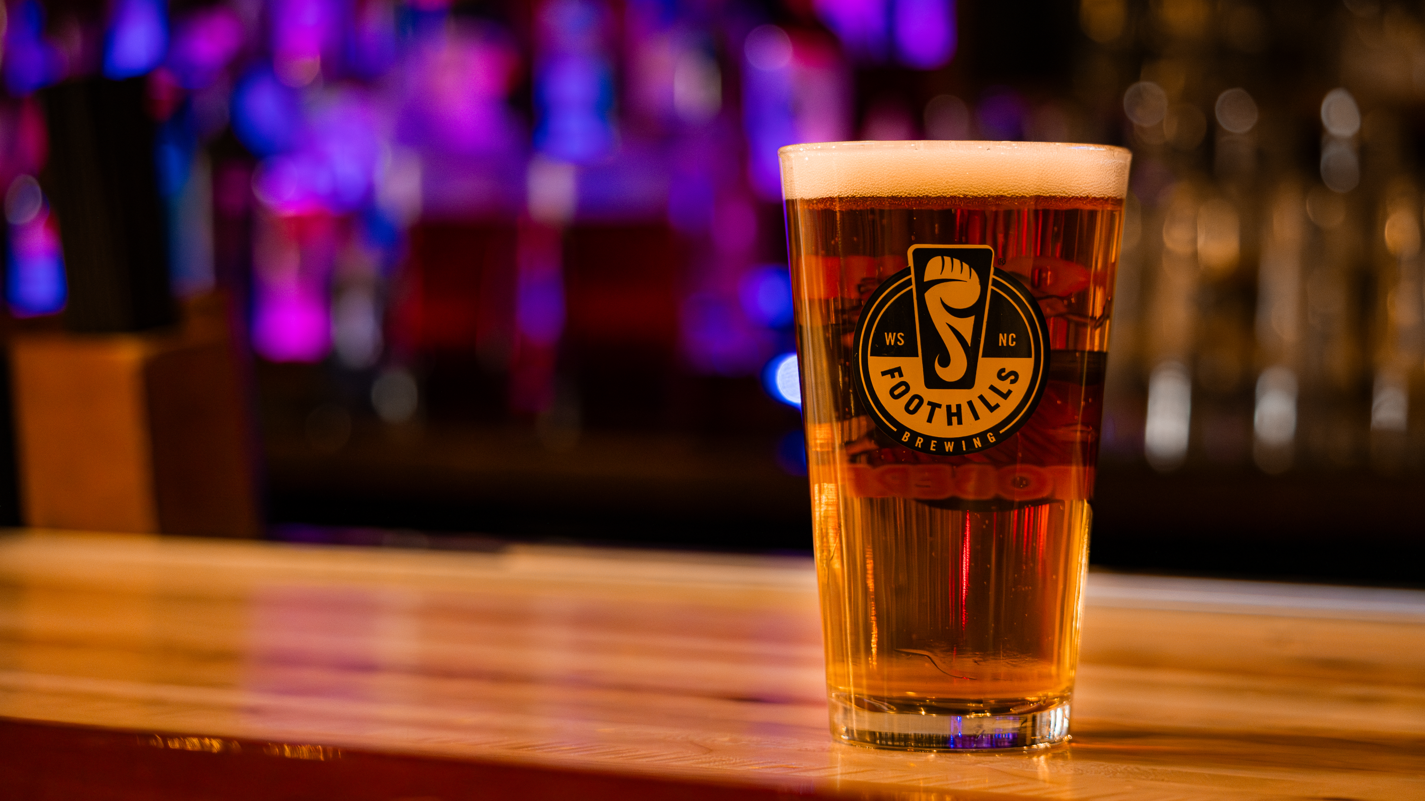 A pint of beer in a Foothills Brewing pint glass on the bar top.