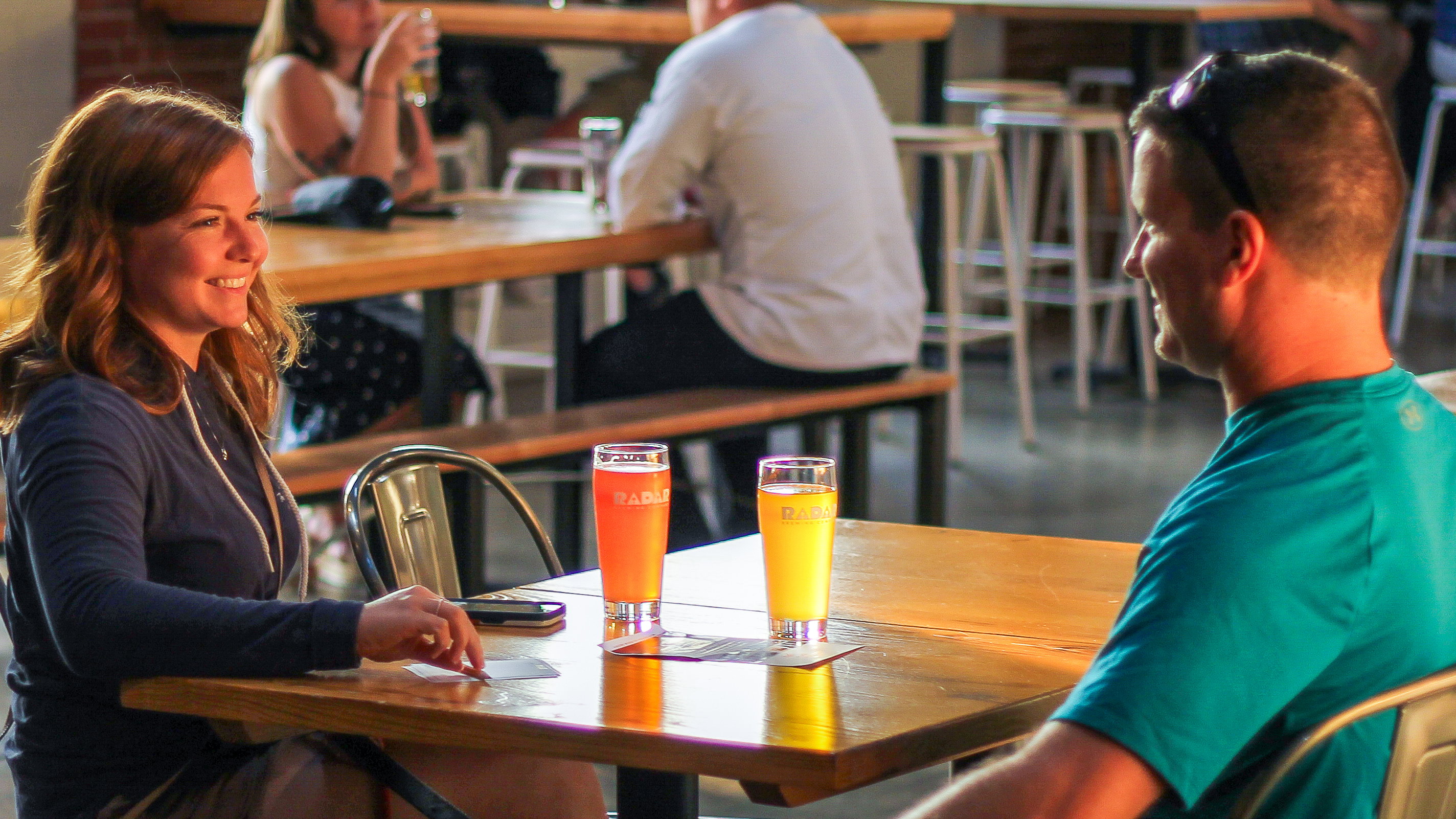 A man and woman sit across from each other, enjoying a beer at Radar Brewing in Winston-Salem.