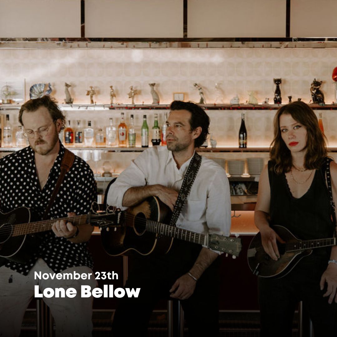 Photo of The Lone Bellow band holding instruments, sitting at a bar