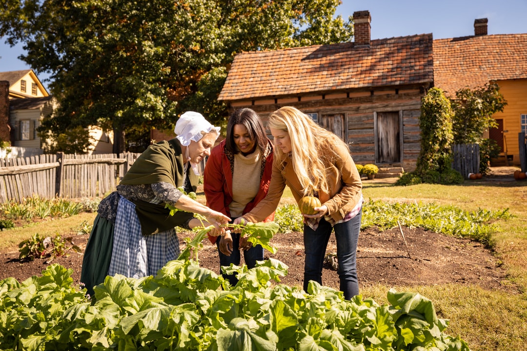 Two women stop to interact with a costumed interpreter in the garden at Old Salem Museums and Gardens in Winston-Salem, North Carolina.