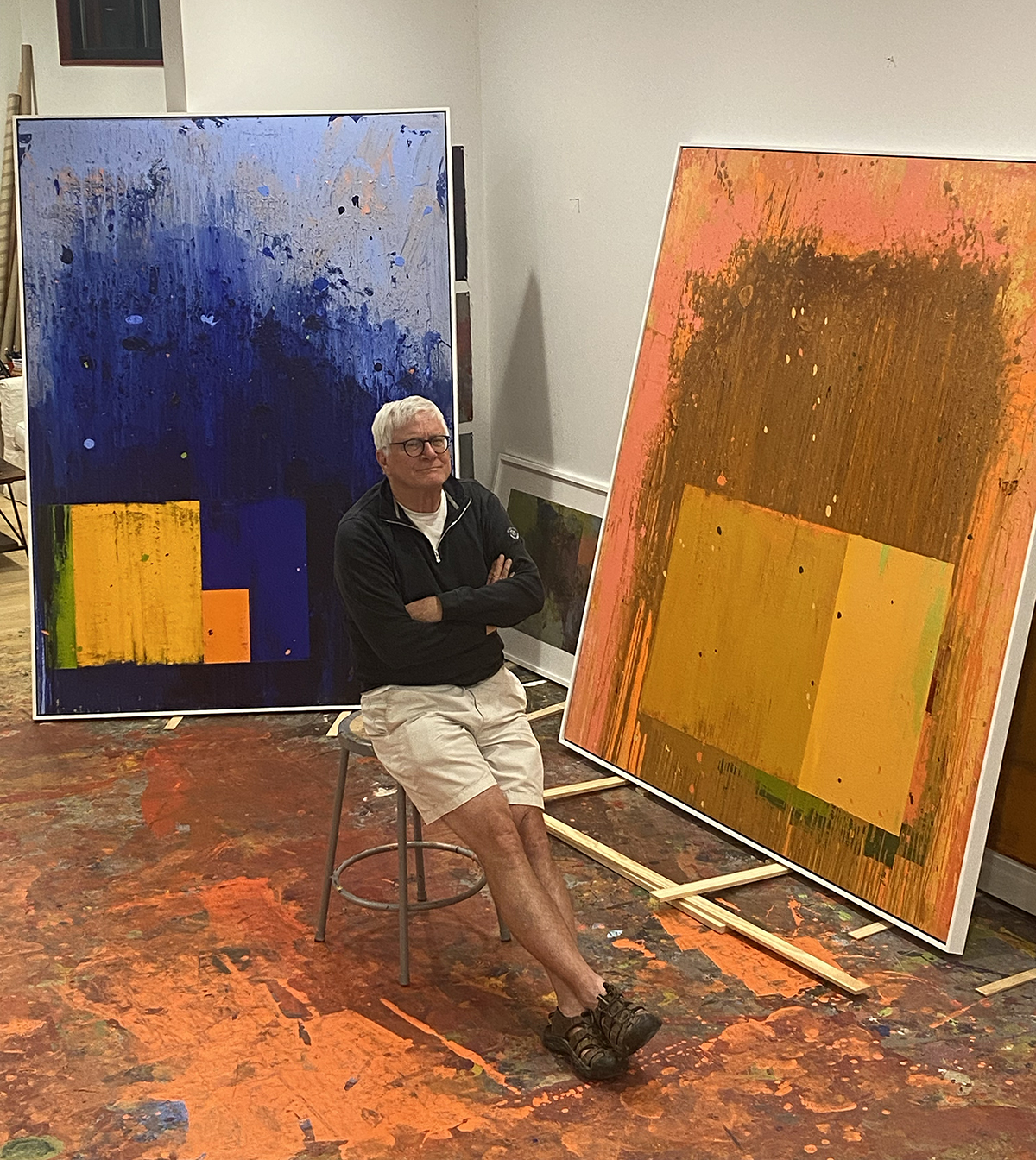 Frank Campion, Winston-Salem local artist, poses in front of two large paintings in his studio.
