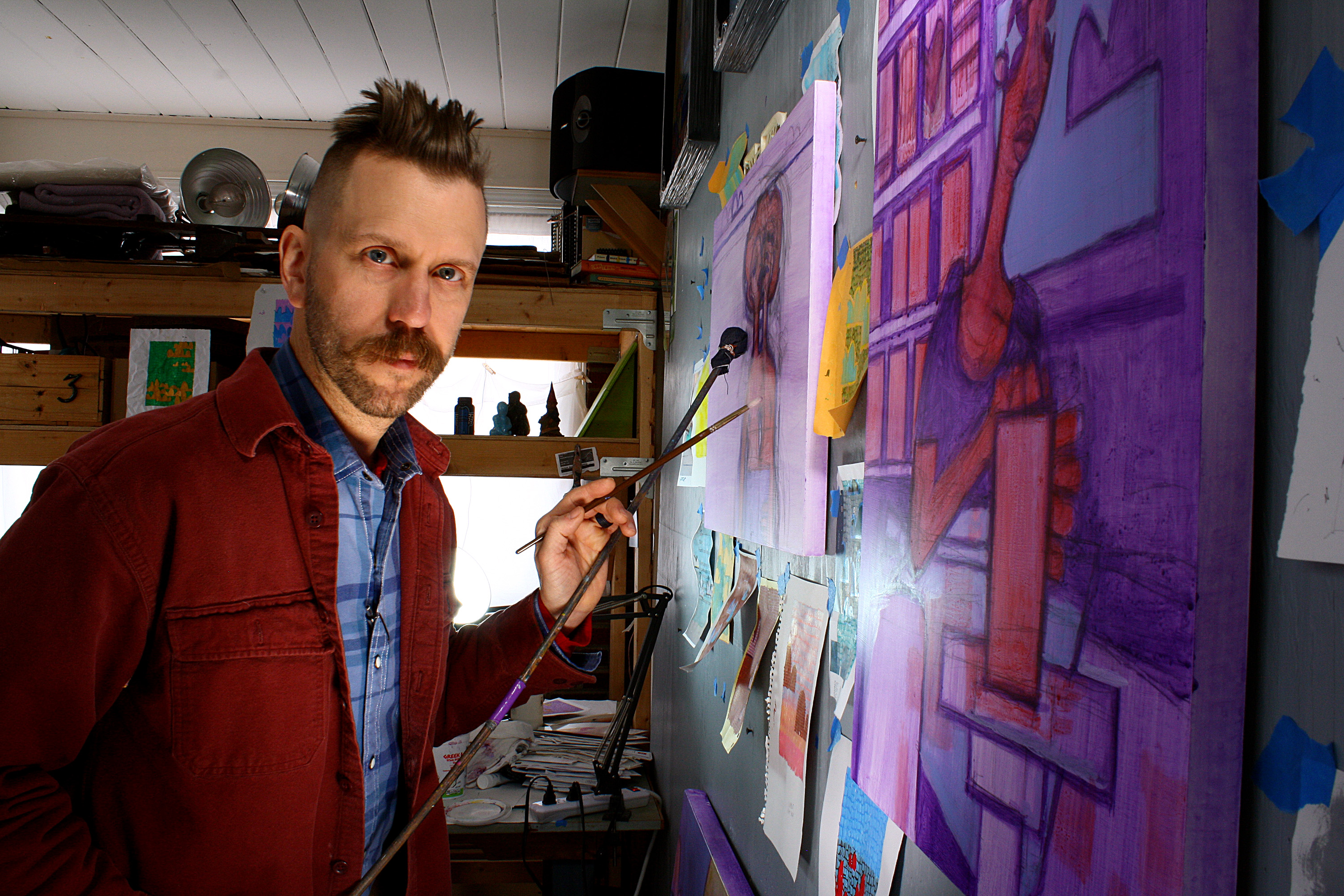 Les poses in his studio alongside one of his paintings.