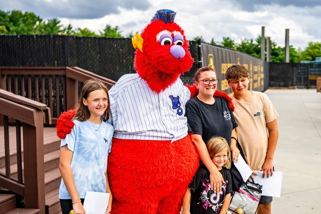 Four children of various ages stop to pose for a photo with Bolt, the Winston-Salem Dash Baseball mascot.
