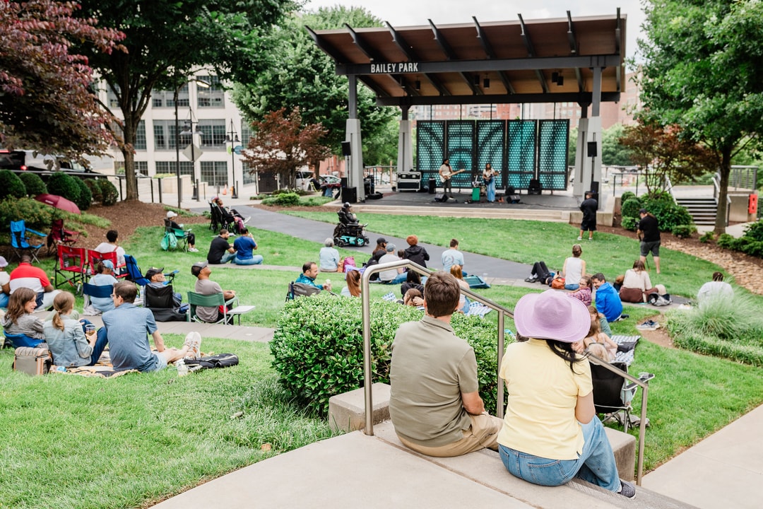 Groups sit on blankets and chairs in Bailey Park watching a small live music performance.