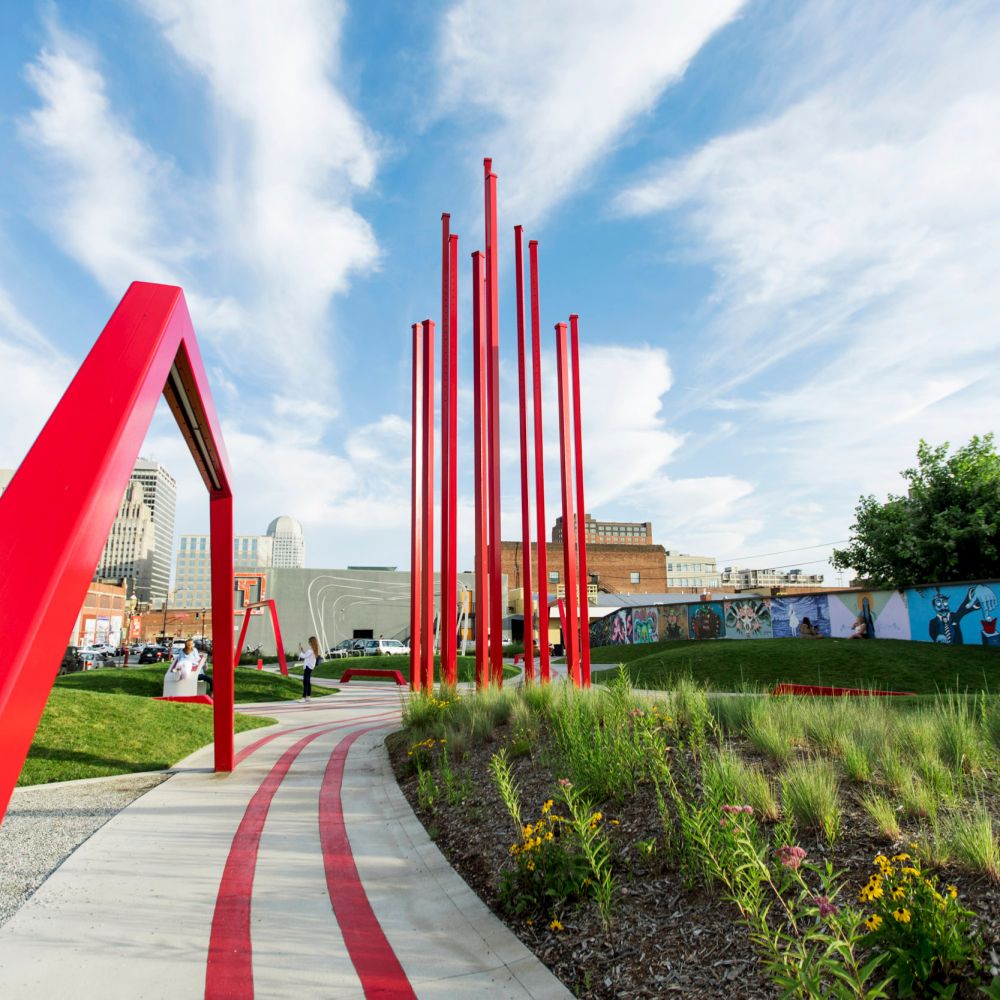 Daytime shot of a large sculpture of multiple red parallel poles in the center of a park.