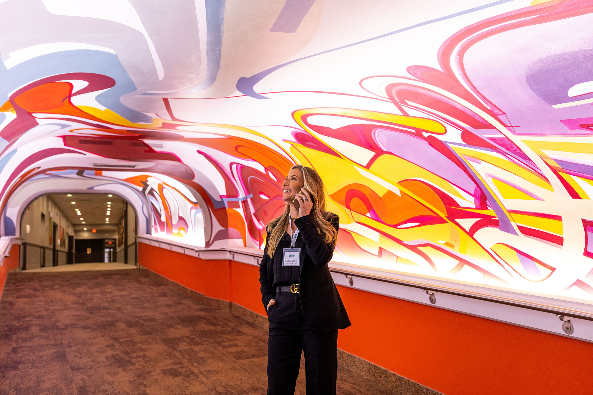 A woman answers a phone call while admiring the artwork in the Benton Convention Center walkway.