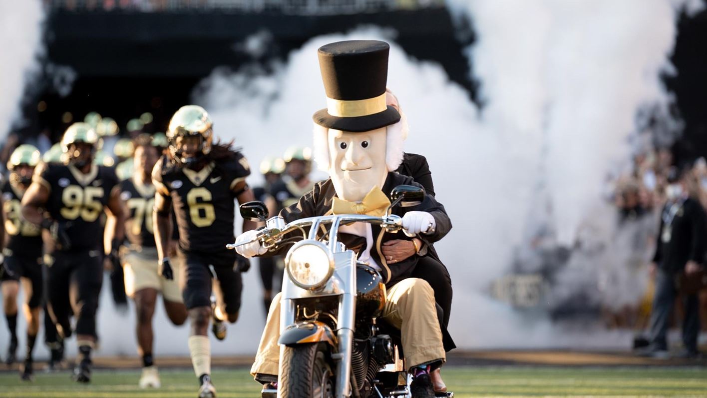 The Demon Deacon- Wake Forest University mascot- rides into the football stadium on his motorcycle, with the football team running in behind him.