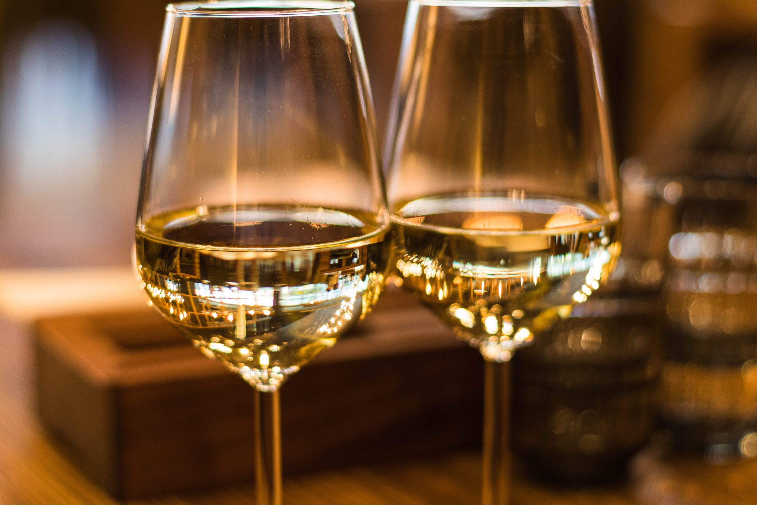 A close up shot of two glasses of white wine pushed together on a table