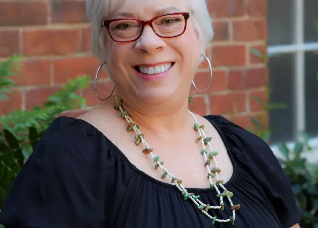 A white-haired woman wearing a black shirt and a long chain necklace
