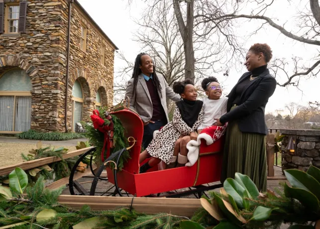 A family of four sits in a sleigh donned with Christmas decorations in front of the Graylyn Estate.