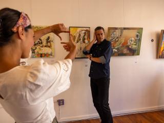 A man poses by framed art on the wall while a woman pretends to take a photo at Visual Index in Winston-Salem.