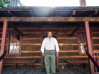 A costumed historical interpreter stands on the porch at Phillips Moravian Church in Old Salem.