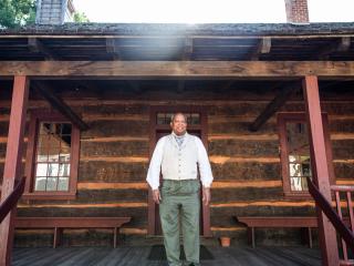 A costumed historical interpreter stands on the porch at Phillips Moravian Church in Old Salem.