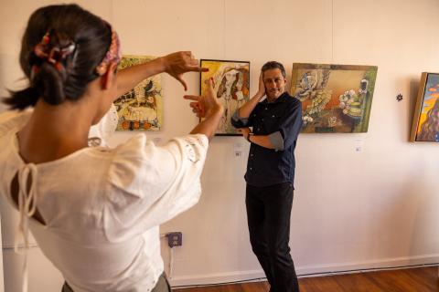 A man poses near an art gallery display while a woman stands in front of him pretending to take a photo at Visual Index in Winston-Salem.