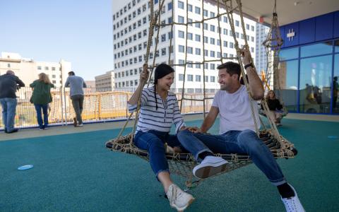 Two adults swinging on a large, circular swing at Kaleideum children's museum in Winston-Salem.