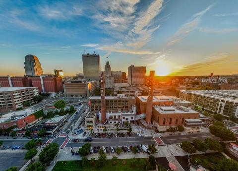 A wide aerial view of the downtown Winston-Salem skyline at sunset.