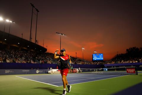 A player at the Winston-Salem Open Tennis Tournament celebrates a win while walking off court, the sunset bright in the background.