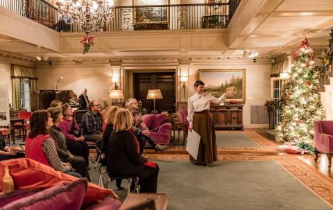 Guide speaking to seated group inside Reynolda House decorated for holidays.