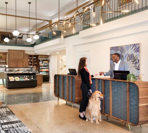 Woman with dog checking in at hotel front desk with receptionist.
