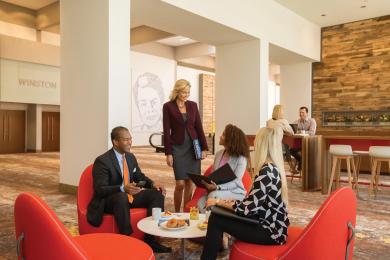 A group of four meeting attendees stop for a brief pre-function meeting in low, red chairs at the Benton Convention Center in Winston-Salem, North Carolina