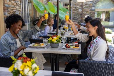 Two women click their wine glasses while sitting across from each other on the Graylyn Estate restaurant patio.
