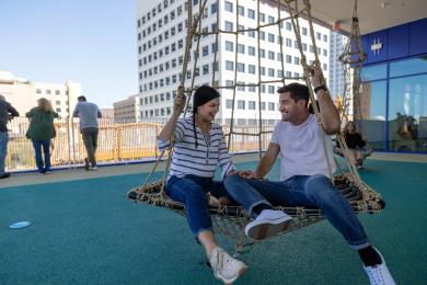 Two adults swinging on a large, circular swing at Kaleideum children's museum in Winston-Salem.
