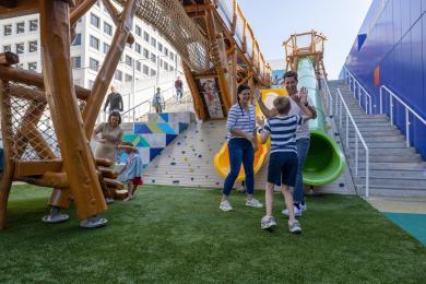 Two adults celebrate and high-five a child after going down the big slide on the rooftop playground at Kaleideum.
