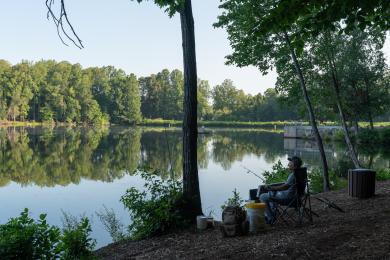 A man sits with his fishing gear in a folding camp chair near the edge of the water in Kernersville Lake Park.