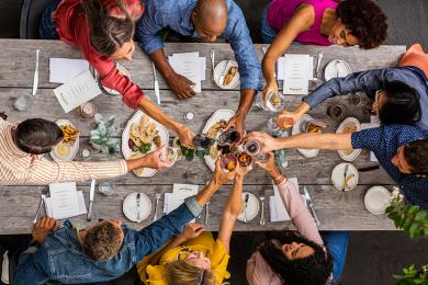 Friends toasting drinks over shared meal at rustic dining table.