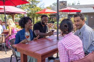 Four people sit at an outdoor dining table at JoLo Winery &amp; Vineyard's Endposts Restaurant near Winston-Salem.