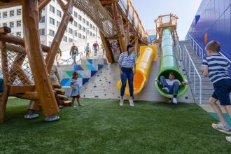 Two parents and their child go down the tube slides on the rooftop playground at Kaleideum Children's Museum in Winston-Salem.
