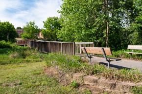 A wooden bench sits on the path near a small foot bridge.